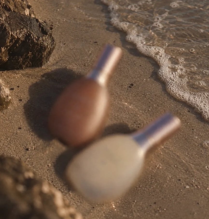Two bottles resting on wet sand beside rocks and a wave